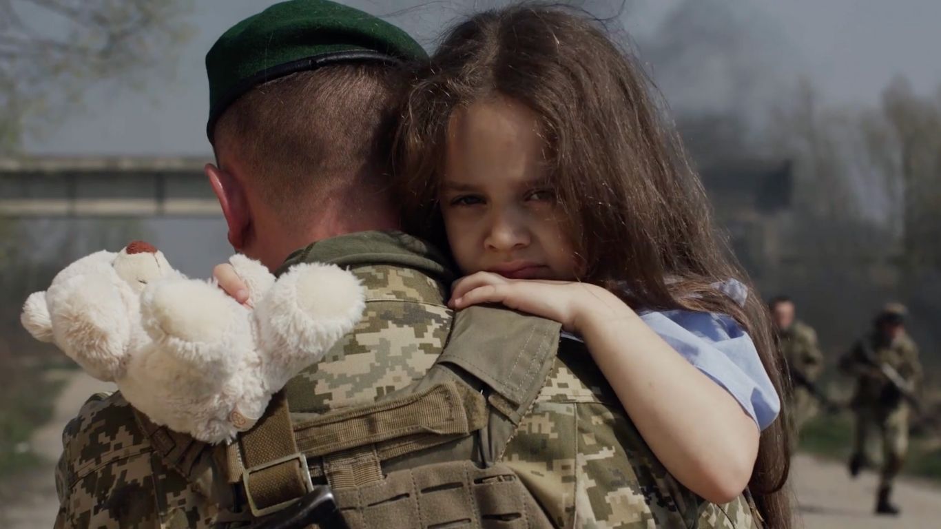 A soldier carrying a small child holding a teddy bear.