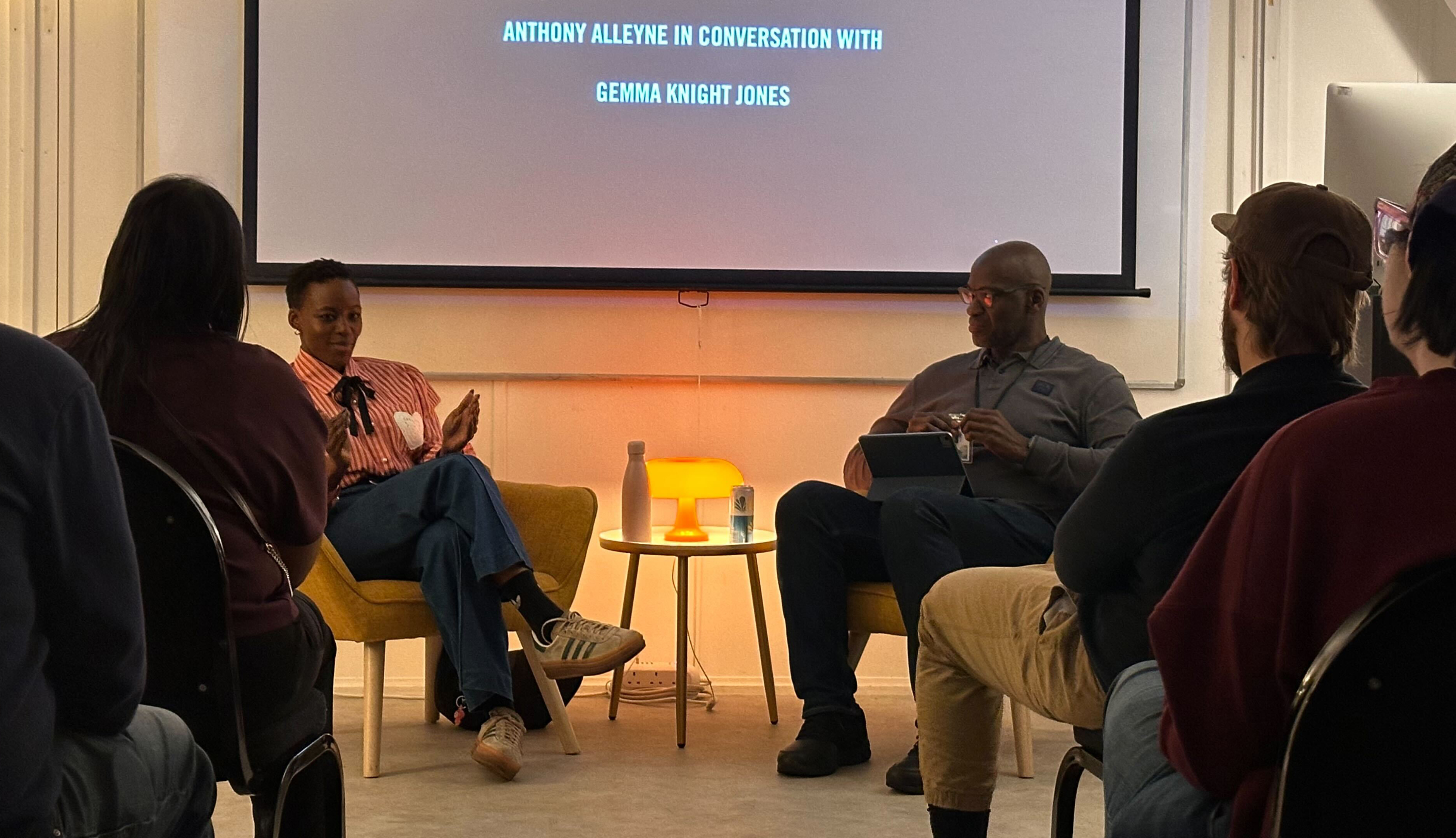 Man and woman sat down talking in front of crowd of students