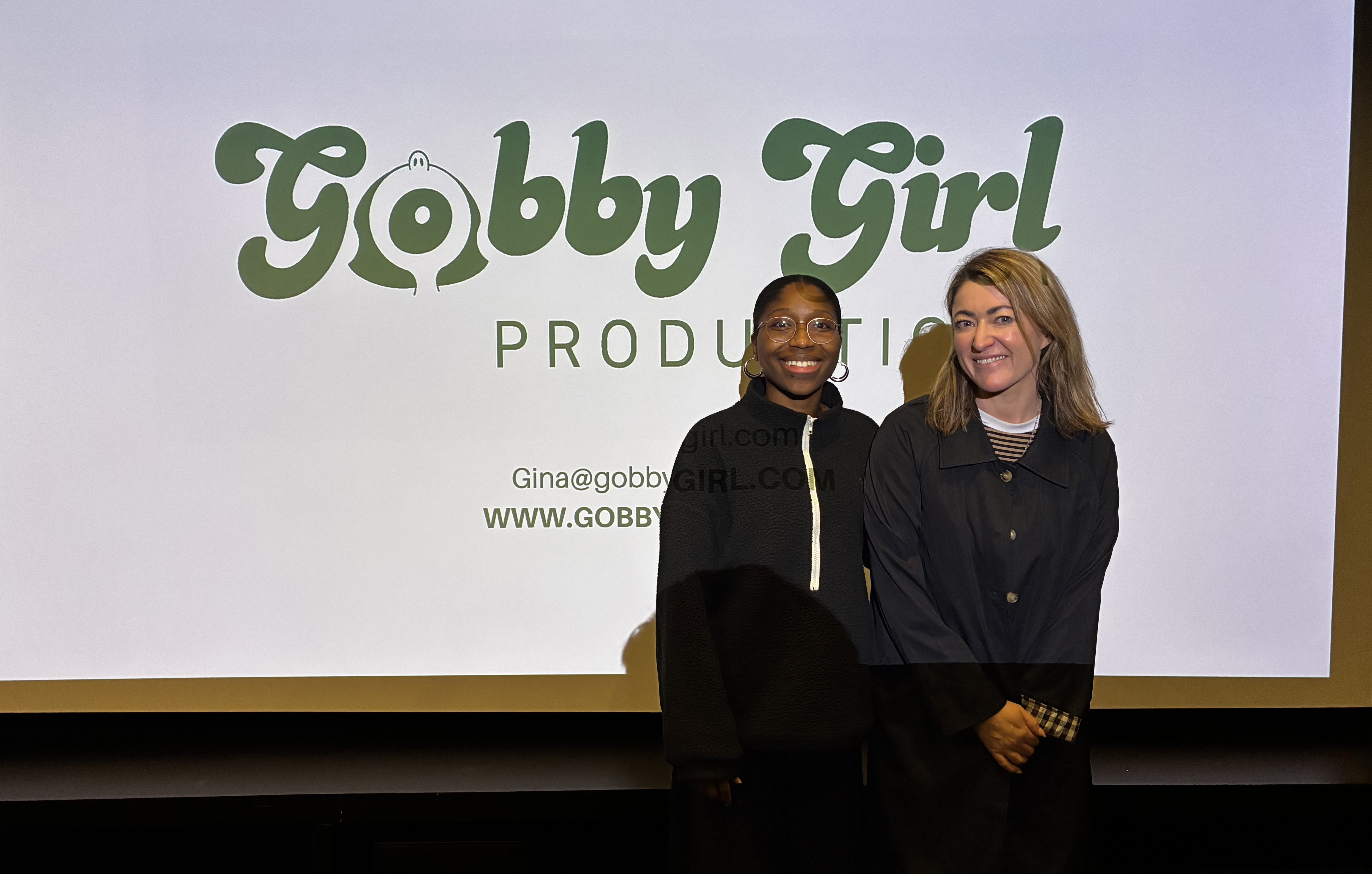 Two women standing in front of cinema screen, smiling