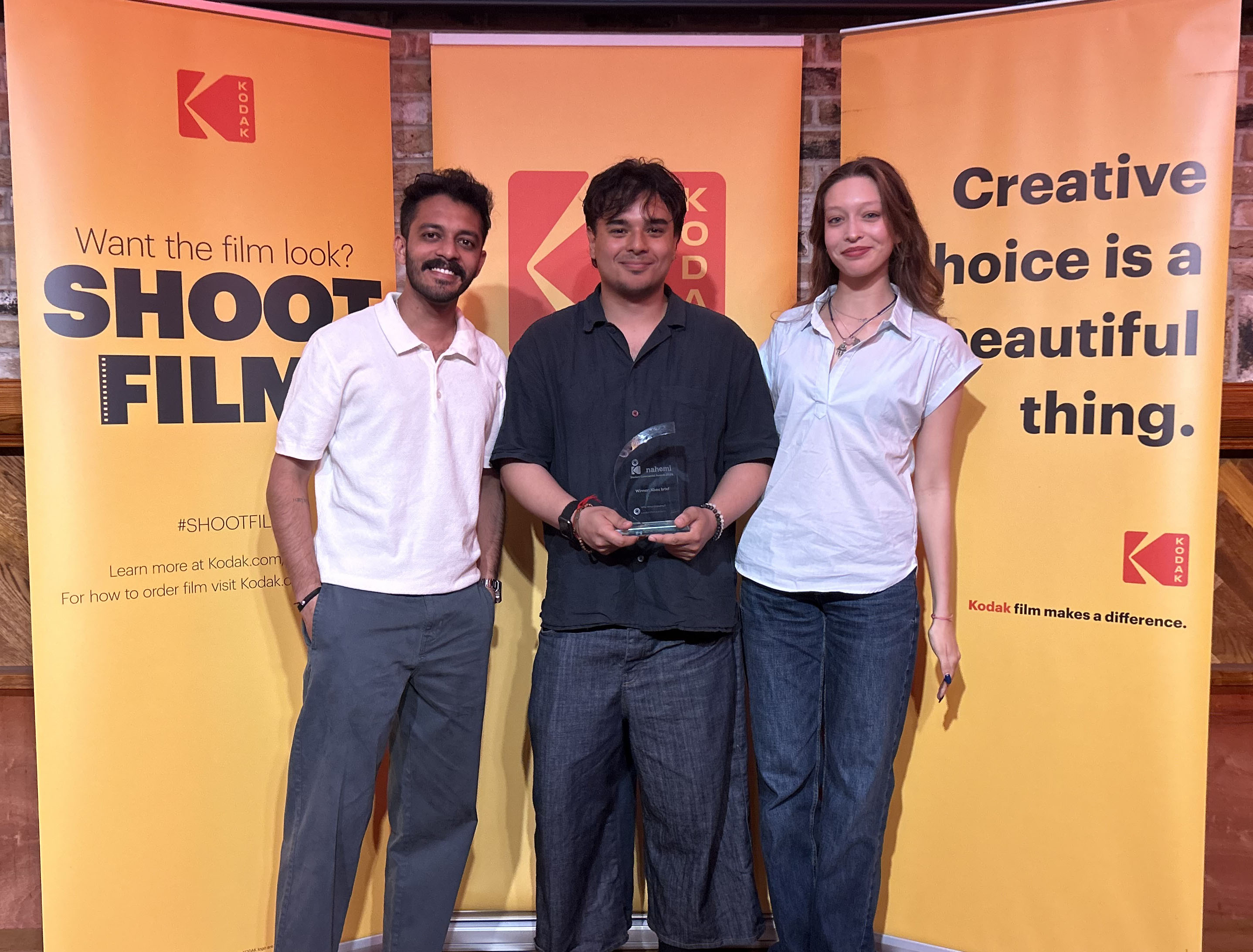 Three smiling students stand in front of Kodak sign, holding their trophy